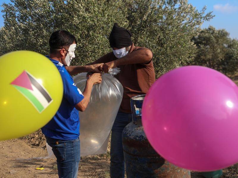 Palestinians in masks attach an incendiary device to balloons before releasing them over Israel.